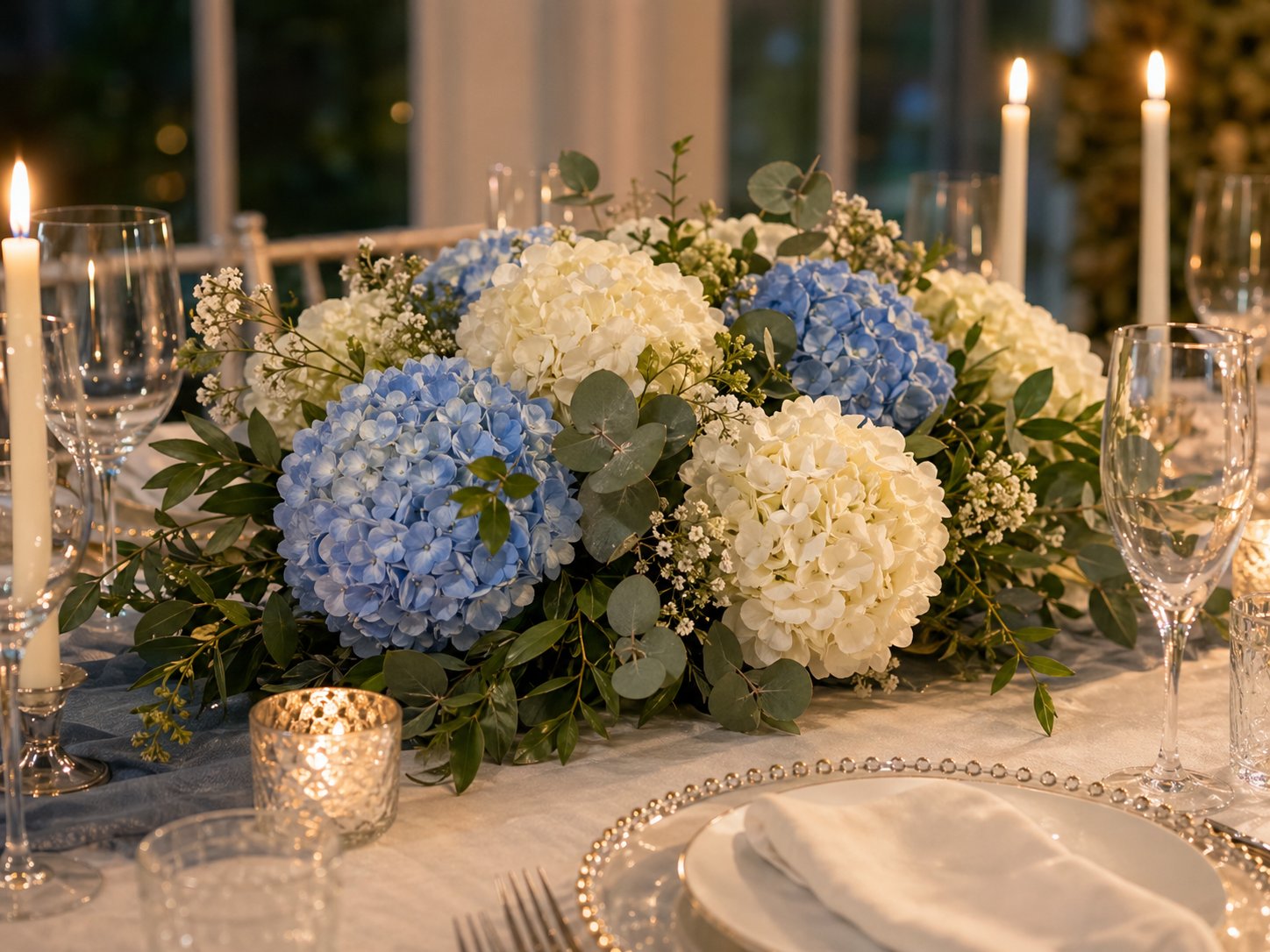 White and blue hydrangeas arranged on an elegant table with candles